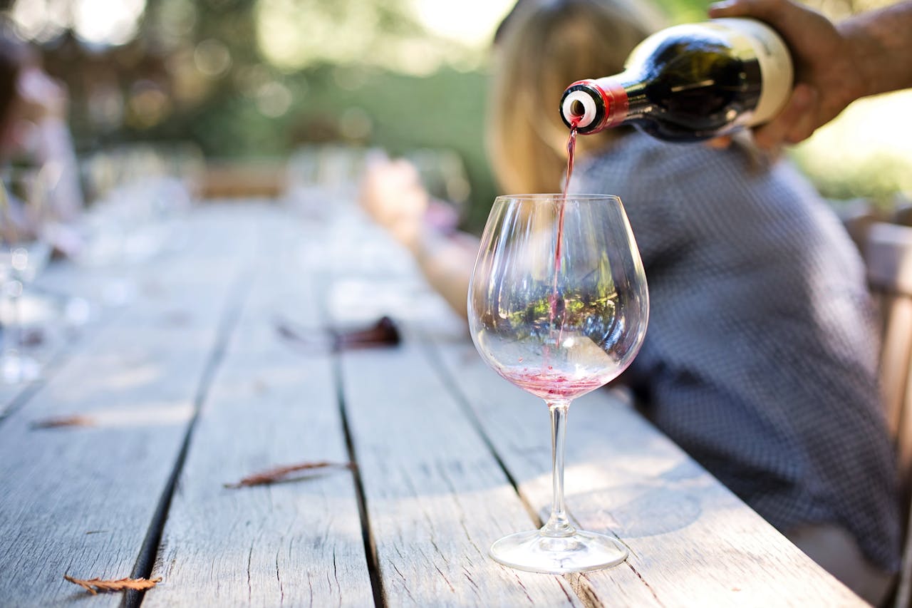The Art of Drawing Readers In: Your attractive post title goes here A hand pouring red wine into a glass on an outdoor table, creating a relaxed atmosphere.